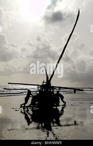 Les pêcheurs brésiliens en poussant leur bateau manuellement vers l'océan pendant le lever du soleil à Uruau, de l'État de Ceara, Brésil. Banque D'Images