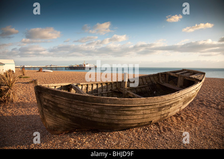 Barque échouée sur une plage de galets avec Brighton, Brighton Pier (est) dans l'arrière-plan, la lumière du soleil du soir Banque D'Images