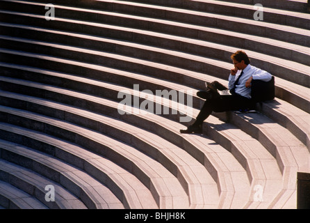 Businessman with cellphone et porte-documents en appui sur le centre-ville de Civic Centre étapes de Los Angeles lire Wall Street Journal Banque D'Images