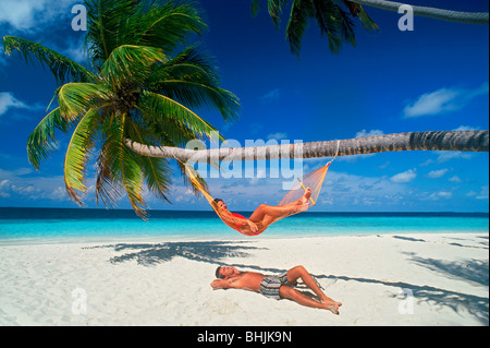 Couple détente avec hamac entre palmiers, ciel bleu et sable blanc Banque D'Images