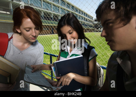 Teenage Girls looking at journal ensemble, garçon qui se tenait à côté de regarder Banque D'Images