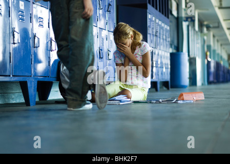 Femme junior high student sitting on floor tenant la tête dans les mains, garçon debout à proximité d'un air suffisant Banque D'Images