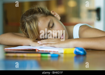 Preteen girl resting head, siestes sur les armes portées au livre ouvert Banque D'Images