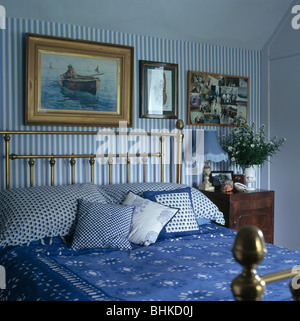 Ancienne peinture sur mur au-dessus de lit en laiton antique avec coussins bleu et couvercle-lit dans chambre avec papier peint à rayures blanc +bleu Banque D'Images