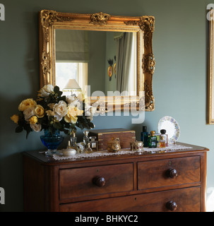 Close-up d'un grand miroir doré au-dessus de vase de roses jaunes sur la poitrine en acajou antique-de-tiroirs dans une chambre bleu pâle Banque D'Images