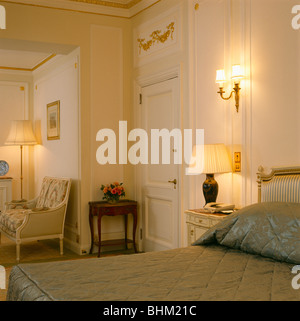 Wall-lumière au-dessus de la lampe allumée sur la table de chevet en crème traditionnelle villa chambres avec couette sur lit Banque D'Images