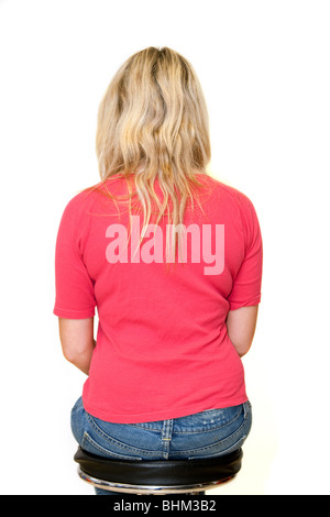 Adolescente blonde assise sur un tabouret avec son dos à l'appareil photo Banque D'Images