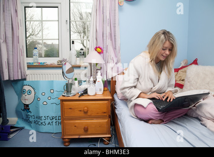 Adolescente blonde en utilisant son ordinateur portable dans sa chambre à coucher Banque D'Images