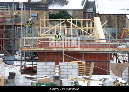 Les constructeurs travaillent sur des échafaudages dans un nouveau site maisons sur un matin d'hiver froid. Banque D'Images