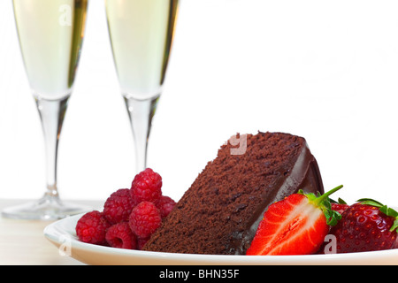 Une assiette de gâteaux au chocolat, les framboises et les fraises tranchées avec flûte deux verres de champagne dans l'arrière-plan. Banque D'Images