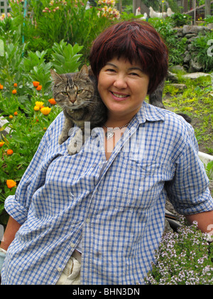 Femme eurasienne mature en bonne santé (chinoise / italienne) dans son jardin avec un chat de compagnie sur son épaule Banque D'Images