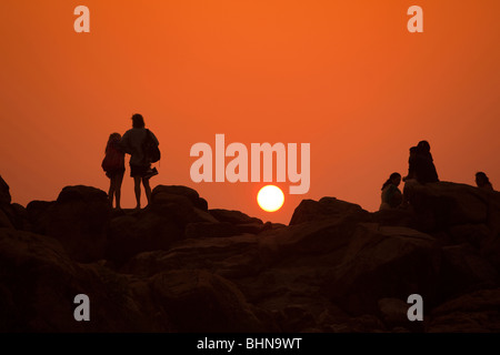 L'Inde, le Kerala, Kovalam, Lighthouse (Adam), les visiteurs de la plage au coucher du soleil sur les rochers Banque D'Images