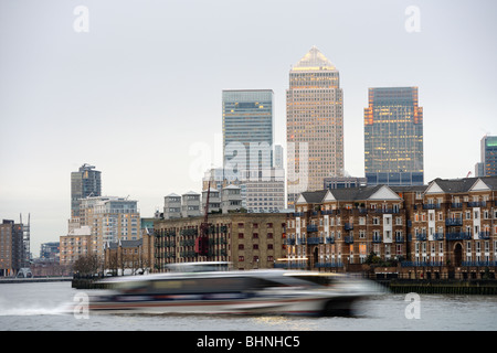 Riverbus rapide remontant la Tamise, Londres, Angleterre, Royaume-Uni, avec Canary Wharf en arrière-plan, au crépuscule Banque D'Images