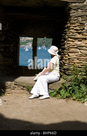 Une femme âgée de 60 ans dans l'élégant quartier de vêtements blancs et hat se trouve dans château fenêtre à voiliers dans la rivière fowey Banque D'Images