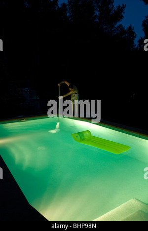 Vue d'un homme seul debout sur le bord d'une piscine la nuit allume la nettoyer à l'aide d'un filet Banque D'Images