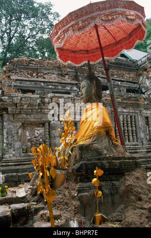 Statue de Bouddha drapé d'or tissu châle sous un parasol de couleur rose avec Vat Phu Champassak en arrière-plan, Champassak, Laos Banque D'Images