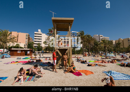 Les jeunes se détendre sur la plage d'El Arenal Majorque, avec en arrière-plan l'arrière-plan lifeguard de palmiers et d'hôtels Banque D'Images