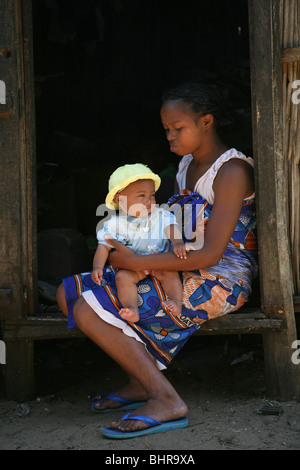 Une femme est assise à la porte de sa maison dans un village à Madagascar avec son bébé sur son genou, l'Afrique Banque D'Images