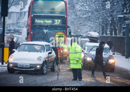 Une route très fréquentée est visible lors d'une douche de neige que le trafic s'accumule aux feux de circulation et les piétons au 76200 Banque D'Images