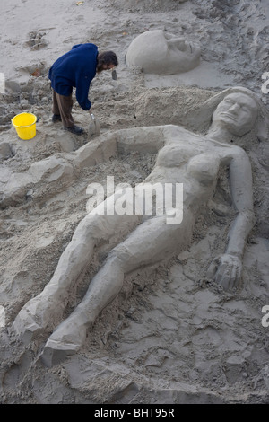 Un sculpteur façonne la forme féminine d'une grande femme de sunbather sable sur l'estran de la Tamise sur la rive sud de Londres. Banque D'Images