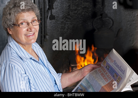 Femme assise par le gîte idéal pour lire un journal avec une lueur dans les yeux Banque D'Images