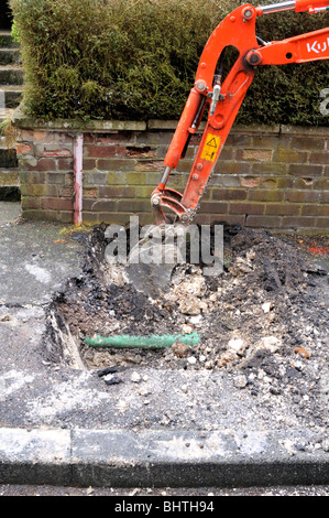 Mini digger creuser dans la chaussée pour remplacer le tuyau de gaz. Banque D'Images