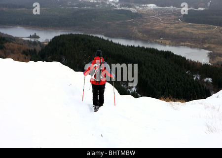 Walker descendre Ben A'une dans la neige de l'hiver avec le Loch Achray ci-dessous Banque D'Images