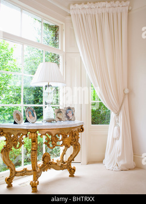 Recouvert de marbre antique gilt table console en baie vitrée avec rideaux crème Banque D'Images