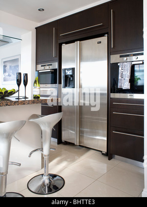 Les tabourets Bombo en acier dans une cuisine moderne de style américain avec grand réfrigérateur-congélateur en acier inoxydable à haute silhouette noire unité équipé Banque D'Images
