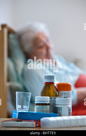 CORONAVIRUS covid-19 dame âgée se reposant malade dans son lit avec une variété de médicaments et de distributeurs en premier plan Banque D'Images