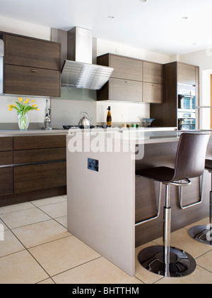 Les tabourets en cuir noir et chrome au bar de petit-déjeuner sur l'unité de l'île de cuisine moderne avec mobilier en bois équipés d'unités Banque D'Images