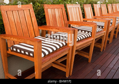 Une ligne de chaises en bois de teck avec des coussins à rayures noir et blanc. Banque D'Images