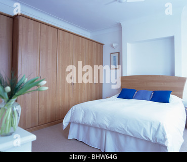 Grande armoire en bois clair dans un style moderne avec des coussins bleu et blanc sur lit couette Banque D'Images