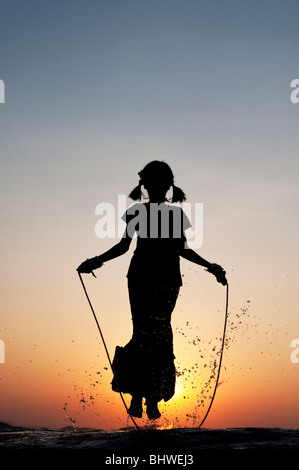 Silhouette d'une jeune Indienne en sautant dans l'eau au coucher du soleil. L'Inde Banque D'Images