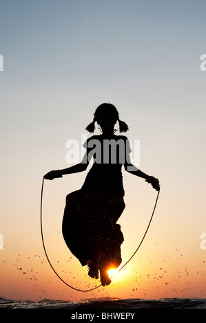 Silhouette d'une jeune Indienne en sautant dans l'eau au coucher du soleil. L'Inde Banque D'Images