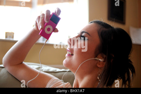 Jeune femme de détente à la maison écouter de la musique sur un Apple iPod nano rose périphérique de stockage Banque D'Images