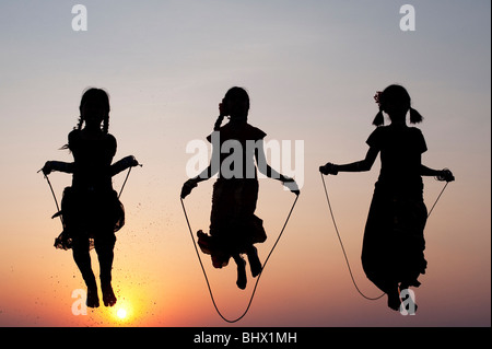 Silhouette de jeunes filles indiennes en sautant dans l'eau au coucher du soleil. L'Inde Banque D'Images