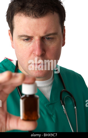 Man wearing scrubs medical stéthoscope et holding et à la recherche d'une petite bouteille de pilules Banque D'Images