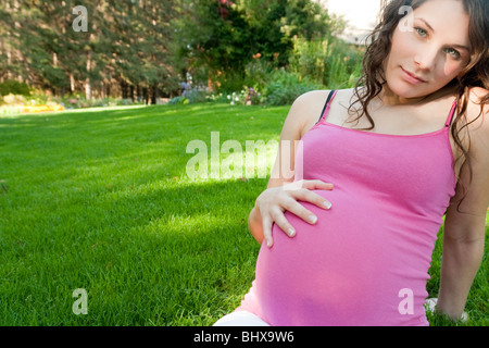 Femme enceinte assis sur l'herbe avec la main sur l'Abdomen, Manitoba, Canada Banque D'Images