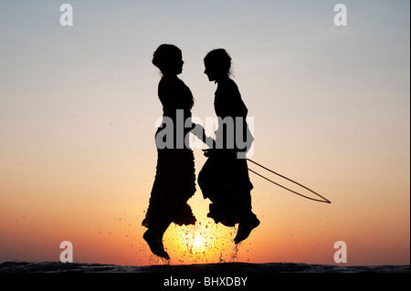 Silhouette de jeunes filles indiennes en sautant dans l'eau au coucher du soleil. L'Inde Banque D'Images