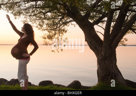 Silohuette de femme enceinte d'atteindre vers le haut, au coucher du soleil, Clear Lake, Manitoba, Canada Banque D'Images