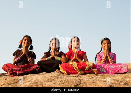 Quatre heureux filles indiennes avec la prière de souhaits pliée mains assis sur un rocher dans l'Inde Banque D'Images