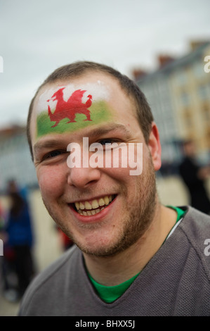 A smiling man avec welsh dragon rouge design de bannières drapeau peint sur son front St Davids Day, Aberystwyth Wales UK Banque D'Images