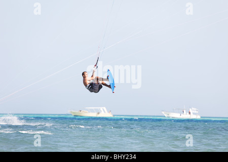 Kiteboarder faire du surf dans l'eau bleu et saute haut dans les airs. Banque D'Images