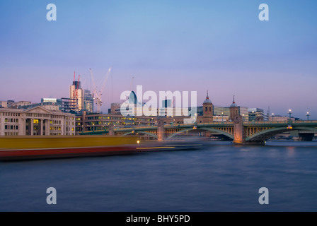 Southwark Bridge dans le centre de Londres à la recherche de la Banque du Sud en début de soirée avec un bateau voyageant passé laissant light trails Banque D'Images