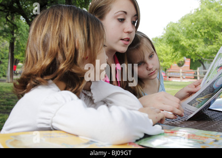 Teen girl reading à deux jeunes filles dans le parc Banque D'Images