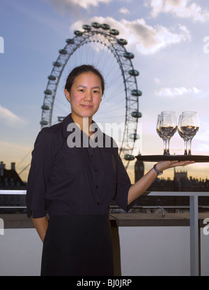 Jeune serveuse asiatique avec des verres à vin sur le plateau en face de London eye Banque D'Images