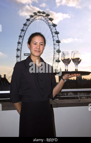 Jeune serveuse asiatique avec des verres à vin sur le plateau en face de London eye Banque D'Images