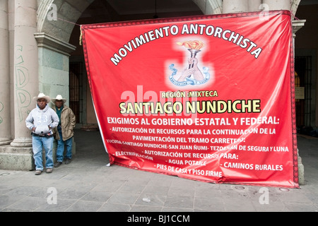 2 campesinos stolid debout à côté signer suspendus à 2 piliers du Palais des Gouverneurs exigeant des services de base pour les Mixtecas Banque D'Images