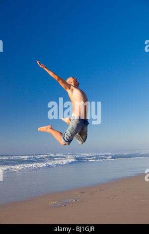Jeune homme sautant sur la plage Banque D'Images